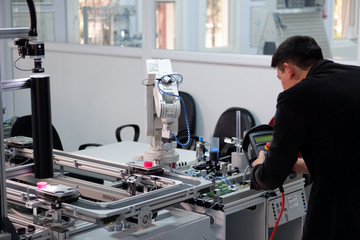 Obraz premium industry 4.0 concept: Man (engineer) is programming robotic arm with control panel (teach pendant) on smart factory production line background. Selective Focus.