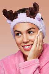 Close-up portrait photo of a dark-haired girl, wearing pink bathrobe and lilac cosmetic bandage...