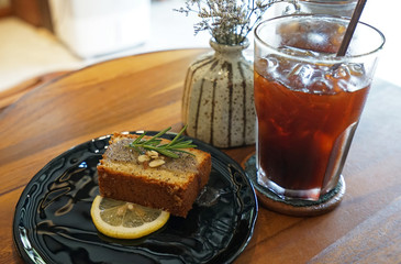 Lemon popy seed cake served with a glass of iced black coffee with stainless steel straw on wooden table