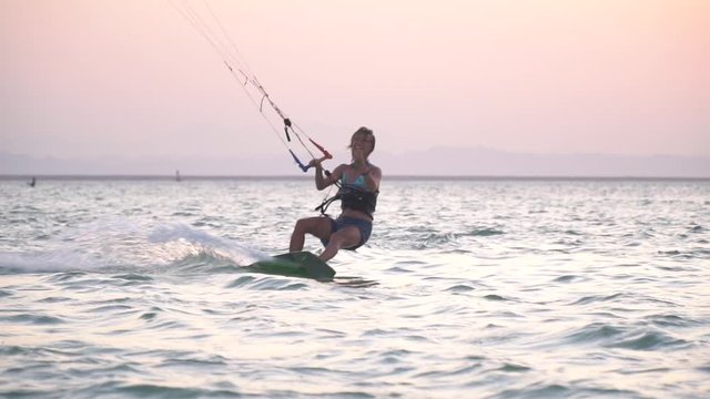 Smiling and laughing woman is kitesurfing in the sea, gliding and tilting