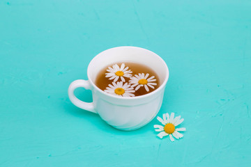 Chamomile tea in a white tea cup, chamomile flowers on the table. Place for text, copy-paste.
