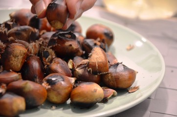 fried chestnuts and peels on a plate. hand takes chestnut. healthy vegetarian food, snacks