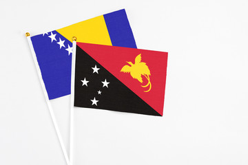 Papua New Guinea and Bosnia Herzegovina stick flags on white background. High quality fabric, miniature national flag. Peaceful global concept.White floor for copy space.