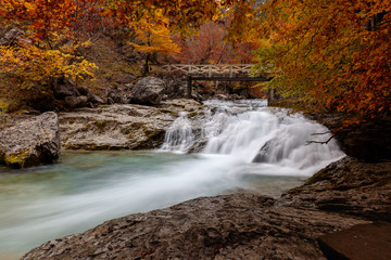 Water cascade going under a bridge in an autumnal forest