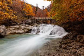 Water cascade going under a bridge in an autumnal forest