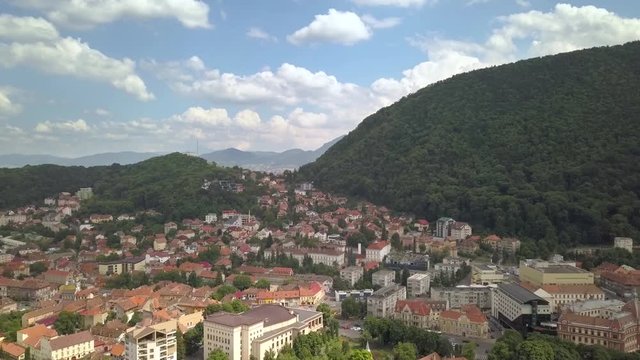 Aerial view of Brasov city, medieval town situated in Transylvania, Romania. Old architecture surrounded with big Carpathian mountains covered with dense green forest.