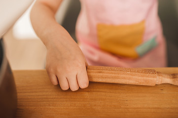 children's hand holds a rolling pin on a wooden table