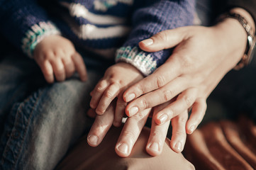 hands of parents hold baby's hand on a background of blue knitted warm clothes