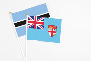 Fototapeta premium Fiji and Botswana stick flags on white background. High quality fabric, miniature national flag. Peaceful global concept.White floor for copy space.
