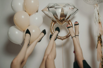  legs of girls in black shoes lie upside down on a light background with gold and white balloons...