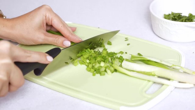 Woman Hand Cutting a Fresh Green Onions on a Plastic Cutting Board on White Tabletop, Concept of Cooking at Home