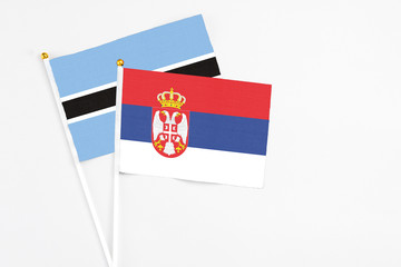 Serbia and Botswana stick flags on white background. High quality fabric, miniature national flag. Peaceful global concept.White floor for copy space.