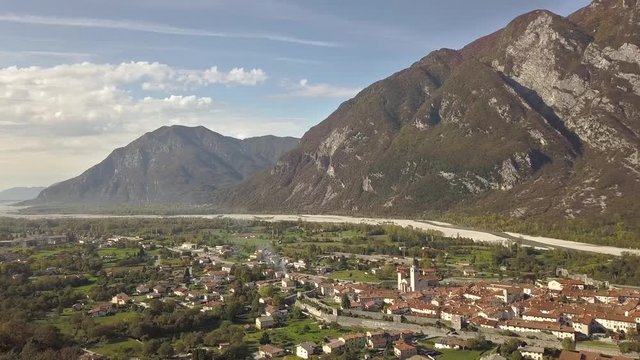 Aerial view of a small historic town Venzone in Northern Italy with red tiled roofs of old buildings and majestic Alps mountains.