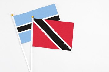 Trinidad And Tobago and Botswana stick flags on white background. High quality fabric, miniature national flag. Peaceful global concept.White floor for copy space.