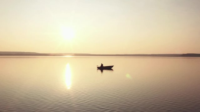 Silhouette of fishermen alone in a boat swimming on a big lake / sunset background - aerial drone view