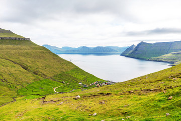 Faroe Islands landscape with green mountains and fjord near a small village.
