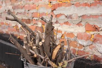 brushwood in a bucket for a stove or fireplace near a brick wall. Old firewood basket on a rustic wooden floor