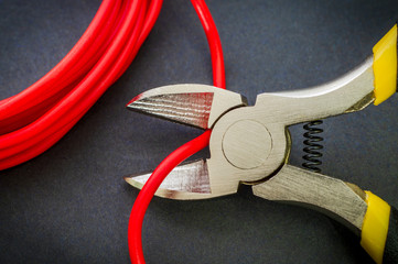 Pliers tool cutting red electric wire closeup on a black background