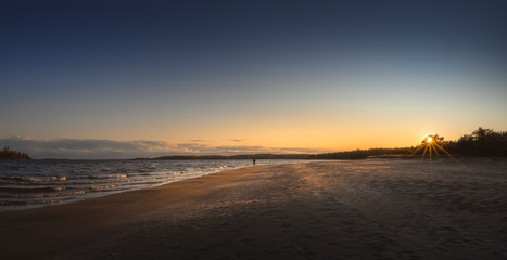 Obraz premium Unrecognizable man walks the beach line. Panorama of northern sand shore
