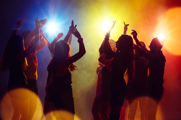 Freedom. A crowd of people in silhouette raises their hands on dancefloor on neon light background....