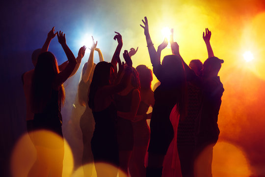 Crazy. A crowd of people in silhouette raises their hands on dancefloor on neon light background. Night life, club, music, dance, motion, youth. Yellow-blue colors and moving girls and boys.