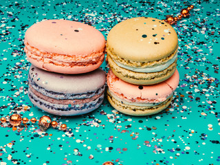 Tasty colorful macaroons on festive green mint background with confetti. Holiday concept. Toned