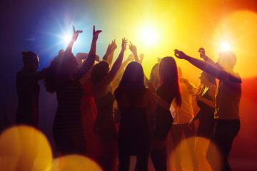 Friends. A crowd of people in silhouette raises their hands on dancefloor on neon light background. Night life, club, music, dance, motion, youth. Yellow-blue colors and moving girls and boys. - obrazy, fototapety, plakaty