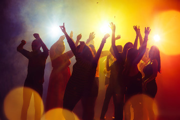 Friendship. A crowd of people in silhouette raises their hands on dancefloor on neon light background. Night life, club, music, dance, motion, youth. Yellow-blue colors and moving girls and boys.