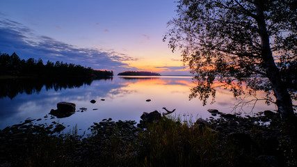 Obraz premium Evening by a lake with trees and beach in the foreground and sunset in the background