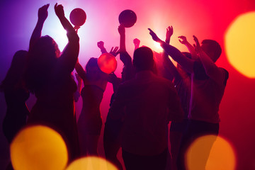 Lauder. A crowd of people in silhouette raises their hands on dancefloor on neon light background....