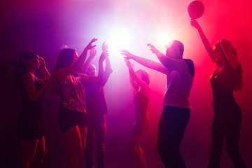 Entertainment. A crowd of people in silhouette raises their hands on dancefloor on neon light...