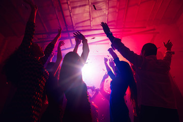 New Year's. A crowd of people in silhouette raises their hands on dancefloor on neon light...