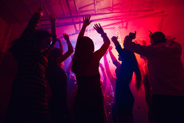 Team. A crowd of people in silhouette raises their hands on dancefloor on neon light background....