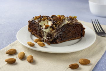 Delicious chocolate cake with raisins, almond and cream. Piece of Chocolate Cake on a Plate. Sweet food. Sweet dessert. Light bakcground. Close up.