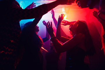 A crowd of people in silhouette raises their hands on dancefloor on neon light background. Night...