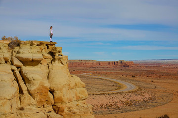 AERIAL: Young woman stands atop a sandstone mountain and observes the desert.