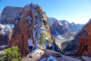 Woman stands proudly and observes the Angel's Landing Trail on sunny winter day. - obrazy, fototapety, plakaty
