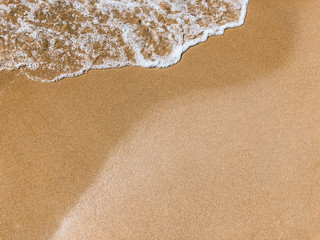 Beach texture. Wave on the sandy beach. Beautiful background with white foam and sand with copyspace