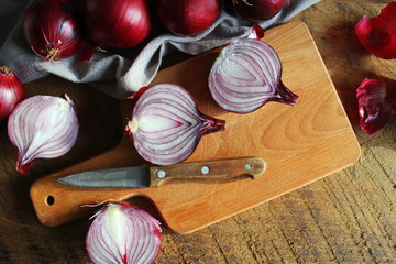 Fototapeta na wymiar Red onions on wooden chopping cutting board on textile napkin over dark wooden rustic texture background. Top view, space for text