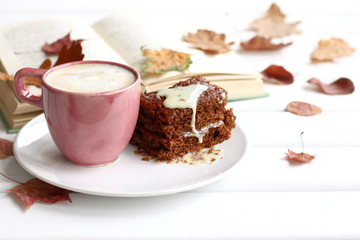 cake with a cup of coffee on a background of books and leaves on the table. sweet warming autumn