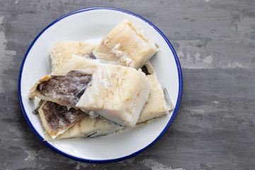 raw cod fish on white dish on ceramic background