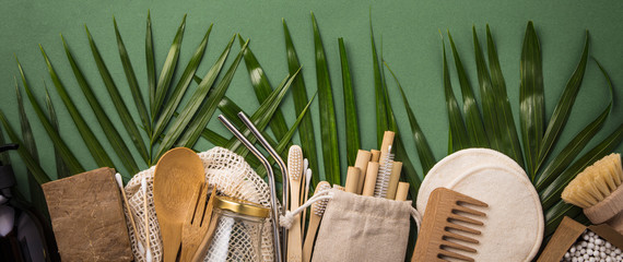 Zero waste concept. Cotton bag, bamboo cultery, glass jar, bamboo toothbrushes, hairbrush and straws on green background