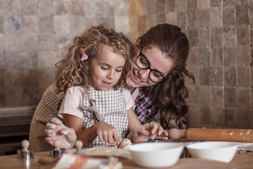 Little curly hair girl making cakes with her mother in kitchen.Mother embrace her child.	
