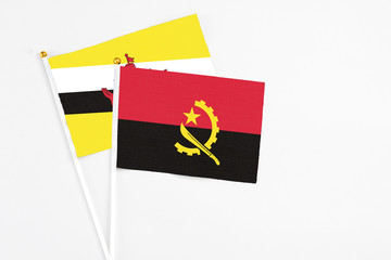 Angola and Brunei stick flags on white background. High quality fabric, miniature national flag. Peaceful global concept.White floor for copy space.