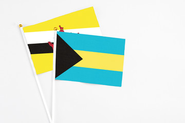 Bahamas and Brunei stick flags on white background. High quality fabric, miniature national flag. Peaceful global concept.White floor for copy space.