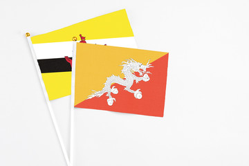 Bhutan and Brunei stick flags on white background. High quality fabric, miniature national flag. Peaceful global concept.White floor for copy space.