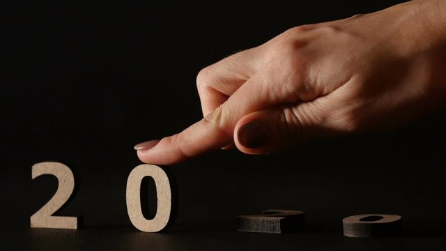 female hand puts numbers 2020 new year instead of the old 2019 by finger, wooden figures on black background, concept change of years slow motion, creative ides