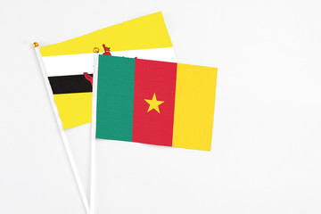Cameroon and Brunei stick flags on white background. High quality fabric, miniature national flag. Peaceful global concept.White floor for copy space.