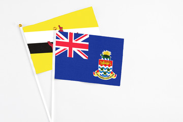 Fototapeta premium Cayman Islands and Brunei stick flags on white background. High quality fabric, miniature national flag. Peaceful global concept.White floor for copy space.