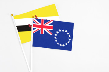 Fototapeta premium Cook Islands and Brunei stick flags on white background. High quality fabric, miniature national flag. Peaceful global concept.White floor for copy space.